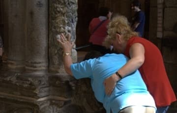 A wheelchair-bound woman is helped to touch the pillar of St. James, just as pilgrims have done for centuries.