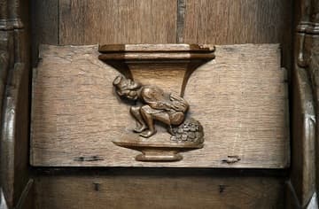 Misericord (c.1480) in the choir of the Oude Kerk, Amsterdam, Netherlands. It illustrates the colorful proverb, "Money doesn't fall out of my arse," of which the more polite equivalent is "Money doesn't grow on trees."