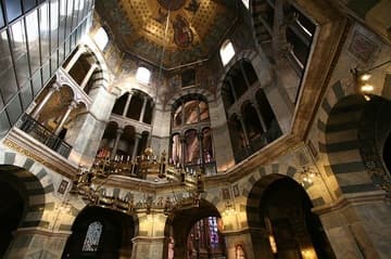 Interior of the Palatine Chapel (786-805), the heart of Aachen Cathedral. The columns of the gallery are purely decorative, not bearing any weight of the arches. Charlemagne had 32 of them shipped from the ancient buildings of Rome and Ravenna. Most of them were looted in the French Revolution but 22 have since been returned and restored to their place in the gallery. The grilles between the pillars were cast of bronze under orders of Charlemagne for this cathedral. They have elaborate patterns with Roman, Celtic and Frankish influences, and are matched in pairs across from each other.