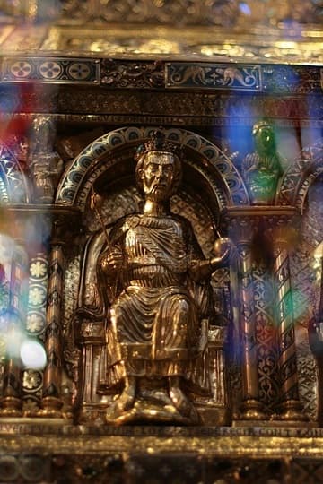 Emperor Otto I on the Shrine of Charlemagne. The golden shrine was made in Aachen in 1215 and still houses the emperor's remains (except for the bits kept in reliquaries in the Treasury). On the front gable Charlemagne is shown enthroned between Pope Leo III and Archbishop Turpin of Reims. The long sides of the shrine depict 16 rulers who donated to the shrine. The other gable has the Virgin Mary flanked by the archangels Gabriel and Michael. Above them are the personified virtues of faith, charity and hope.
