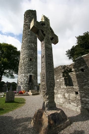 Round tower and West Cross, the tallest cross in Ireland at 6.5m. Dating from the early 10th century, it is more weathered than Muirdach's Cross, especially at the base, leaving only about a dozen of its original 50 panels distinguishable. Monasterboice, Ireland.