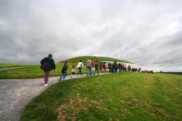A busload of visitors makes the short walk uphill to Newgrange, a prehistoric passage tomb and ceremonial chamber dating from about 3200 BC. Boyne River Valley, County Meath, Ireland.