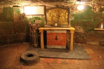 A small altar in the lower room of the Mamertime Prison. The upside-down cross lends the desolate place an extra-sinister air, but that's just the Cross of St. Peter (who was crucified upside down). In the foreground is a spring that Peter is said to have made miraculously spring up so he could baptize his fellow prisoners; the altar relief shows him doing so.