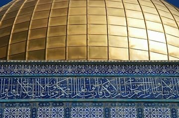 In this closeup of the dome and tiled drum of the Dome of the Rock, one can admire the intricate tilework and second set of Arabic calligraphy. The Arabic is a Quranic verse telling of Muhammad's Night Journey: "Glory be to He Who carried His servant by night, from the Holy Mosque [Mecca] to the Furthest Mosque [Jerusalem], the precincts of which We have blessed so that We might show him some of Our signs. Surely He is the All-Hearing, the All-Seeing." (Sura al-Isra', Qur'an 17:1)