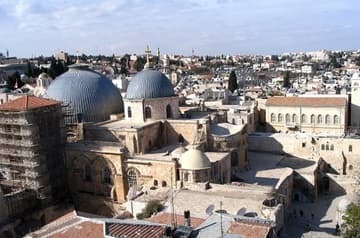View of the Church of the Holy Sepulchre from the Lutheran Church of the Redeemer. On the left is the Crusader facade and entrance courtyard and the truncated Crusader bell tower. The larger blue dome is directly over the tomb of the Christ; the smaller one is over the Catholicon (Greek Orthodox cathedral). The small white dome is near Calvary. On the far right is the roof, which includes the humble structures of Ethiopian Orthodox monks. The dome just seen on the far right is over the Chapel of St. Helen.