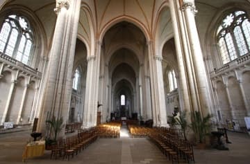 Nave of Poitiers Cathedral, looking east. Dating mainly from the 13th century, the interior is bright and spacious thanks to its lofty Gothic vault (30m high), slender white pillars, wide nave and aisles (30m) and a long vista (100m) down the nave. The corbel tables on the walls are carved with an interesting variety of human heads.