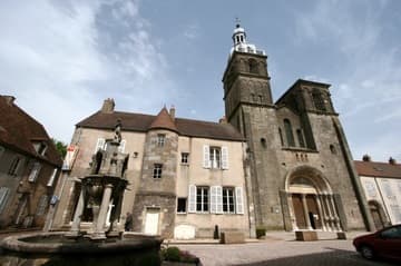 Exterior of Saulieu Basilica, overlooking a small plaza with a fountain.