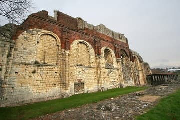North wall of the Norman nave, walled up and converted into a palace for Anne of Cleves, the fourth wife of King Henry VIII, in 1539. The brickwork is part of that Tudor conversion. The stone of the Norman church was imported from Caen in Normandy. To the east (far right of this photo) is a wooden roof protecting a porticus chapel of the original Anglo-Saxon church, which contains burials of abbots.