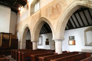 Nave looking northwest, with a view of 13th-century murals on the north arcade: St Christopher (under the window) and the Coronation of the Virgin. Black Bourton, Oxfordshire, England.