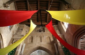 View of the tower arch from the nave, with decorations for a play being held in the church. The three niches above the Early English arch were designed as a background for the figures on the rood beam of the Virgin Mary, Christ, and St. John. Above on each side are murals of angels with shields bearing the Five Wounds of the Passion.