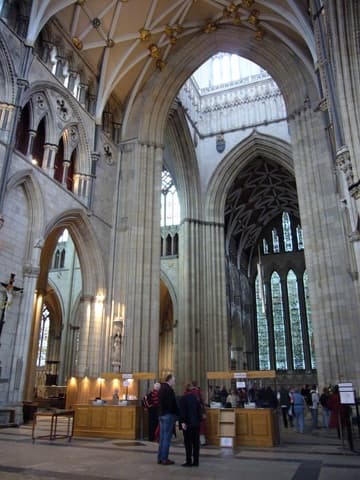 The first look inside York Minster after entering from the south door. This view is free; to pass the wooden desks, you must pay admission. Through the great central arches can be seen the Five Sisters Window, dating from 1250. On our left (not seen) are the entrances to the tower and to the undercroft.