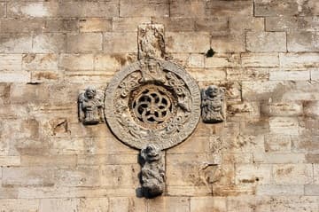 Small oculus with beautifully carved designs, sculptures of angels and some creature, and a weathered Latin inscription on the west facade. 13th century. Ruvo di Puglia Cathedral, Puglia, Italy.