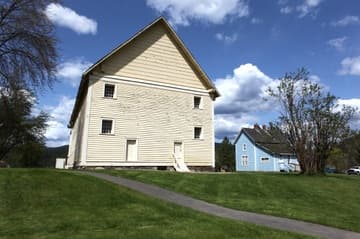 Exterior view of the mission church from south, with the blue Parish House visible on the right. The Sacred Heart Mission near Coeur d'Alene was built 1850-53 by Jesuit missionaries and Native Americans. The church is the oldest building in Idaho. Today it is owned by the Coeur d'Alene tribe and operated by the state as Old Mission State Park.