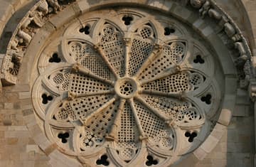 Beautiful rose window on the west facade of Troia Cathedral, dating from 1160-80 and filled with stone screens of Islamic-inspired geometrical designs. Arching around the window are carvings of human and animal figures. Typical Puglian lions keep watch on either side.