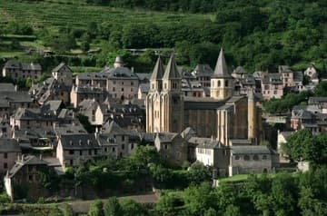 A magnificent view of Conques and its Church of St. Foy, nestled on a thickly wooded slope in southwest France. This photo was taken from a rocky outcrop across the gorge of the River Dourdou, a tributary of the Lot.