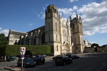 Poitiers Cathedral viewed from northwest in evening sunlight. Flanked by two stout, mismatched towers of the Transitional period (early 13th century), the facade features a Gothic rose window and three sculpted portals. The portals date from the second half of the 13th century and are in the High Gothic style of Amiens and Reims. The tympanums depict the Dormition and Coronation of the Virgin, the Last Judgment, and the life of St. Thomas. The upper part of the facade including the rose window dates from the 14th century. The north transept, with round-headed windows, dates from the late 12th century Romanesque period.