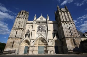 West facade of Poitiers Cathedral in evening sunlight. Flanked by two stout, mismatched towers of the Transitional period (early 13th century), the facade features a Gothic rose window and three sculpted portals. The portals date from the second half of the 13th century and are in the High Gothic style of Amiens and Reims. The tympanums depict the Dormition and Coronation of the Virgin, the Last Judgment, and the life of St. Thomas. The upper part of the facade including the rose window dates from the 14th century.
