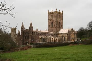 View of St. David's Cathedral from the southwest, showing the west front made of local purple stone, the nave, the south transept, and the tower. St Davids, Wales.